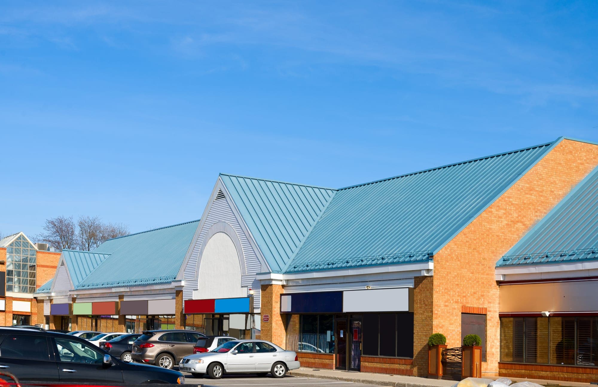 Retail plaza with metal roofs and a car-lined parking lot