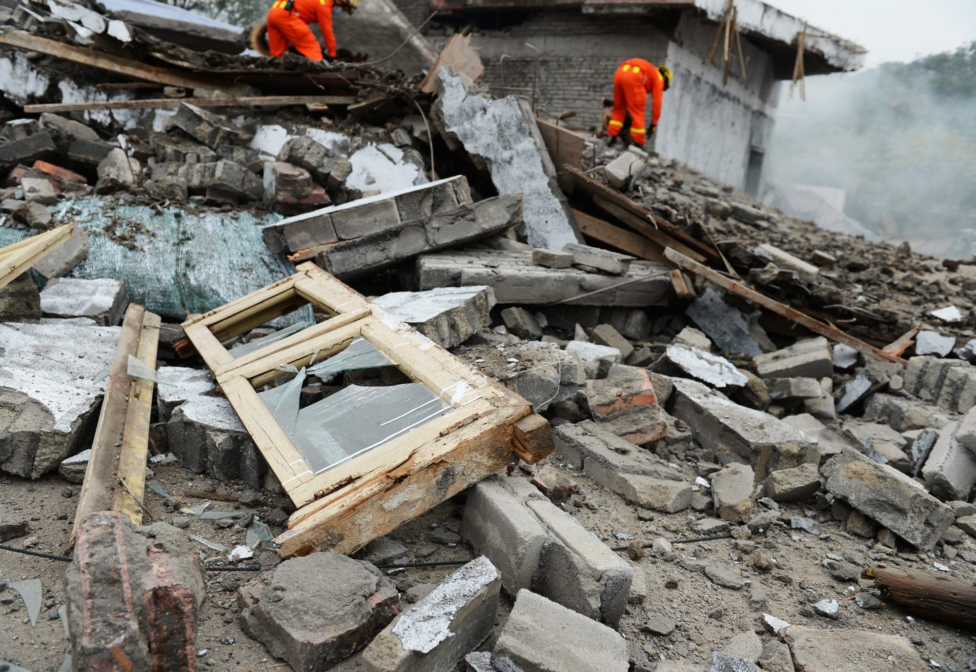 Rescue workers atop the rubble of a collapsed masonry house