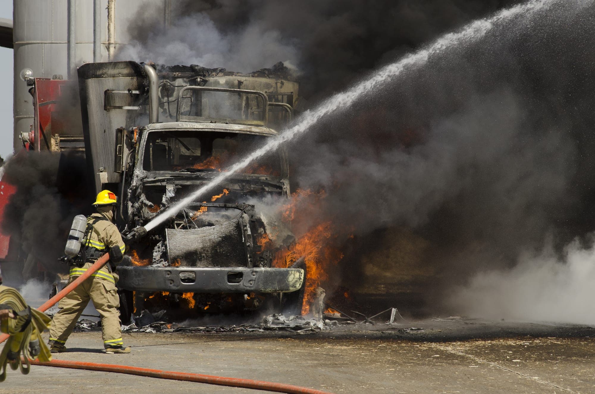 Firefighter hosing a burned box truck amid heavy smoke