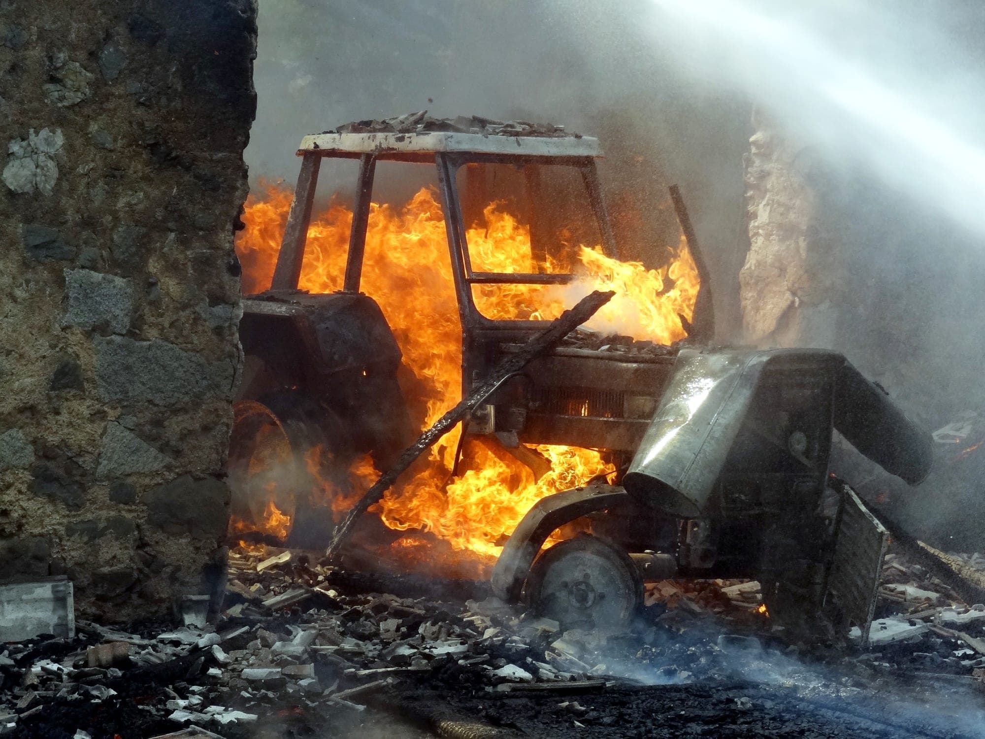 Farm tractor engulfed in flames beside a stone building