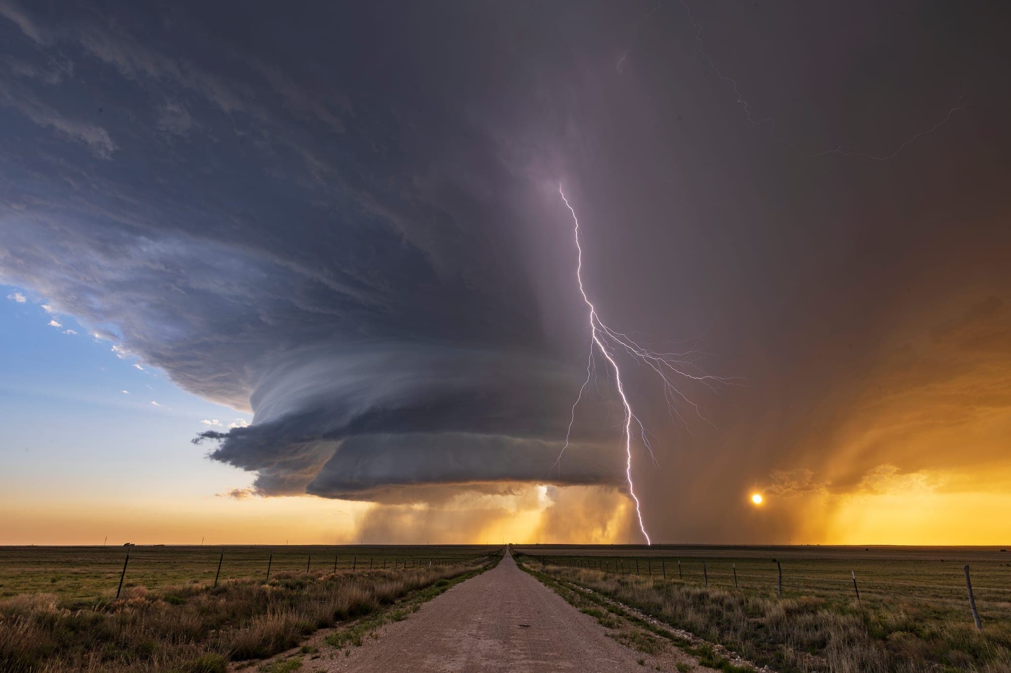Lightning strike beneath a supercell storm over a rural road