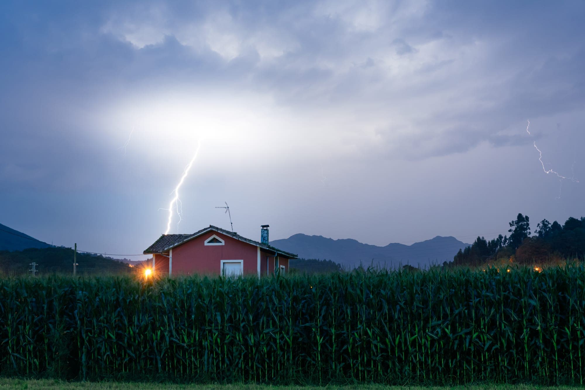 Lightning striking behind a small house beside a cornfield