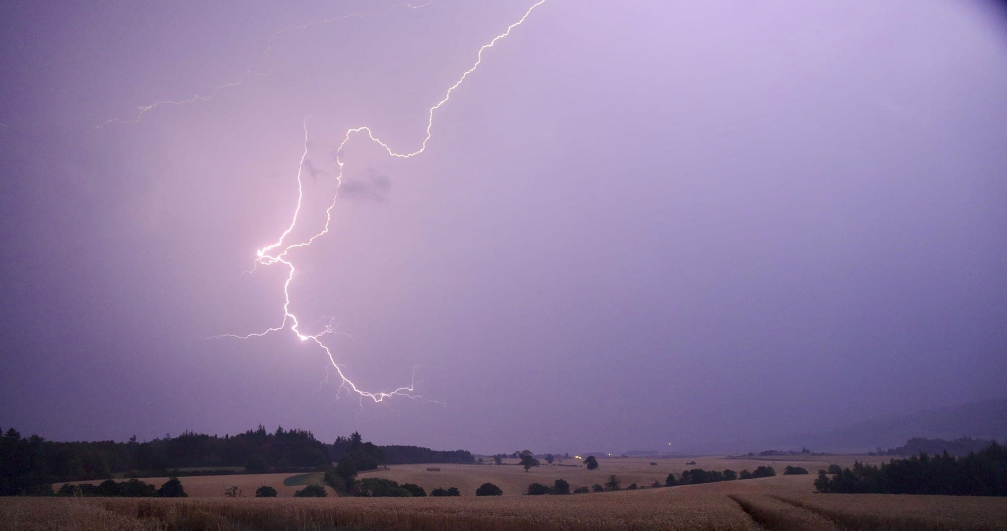 Branched lightning crossing a purple storm sky over farmland