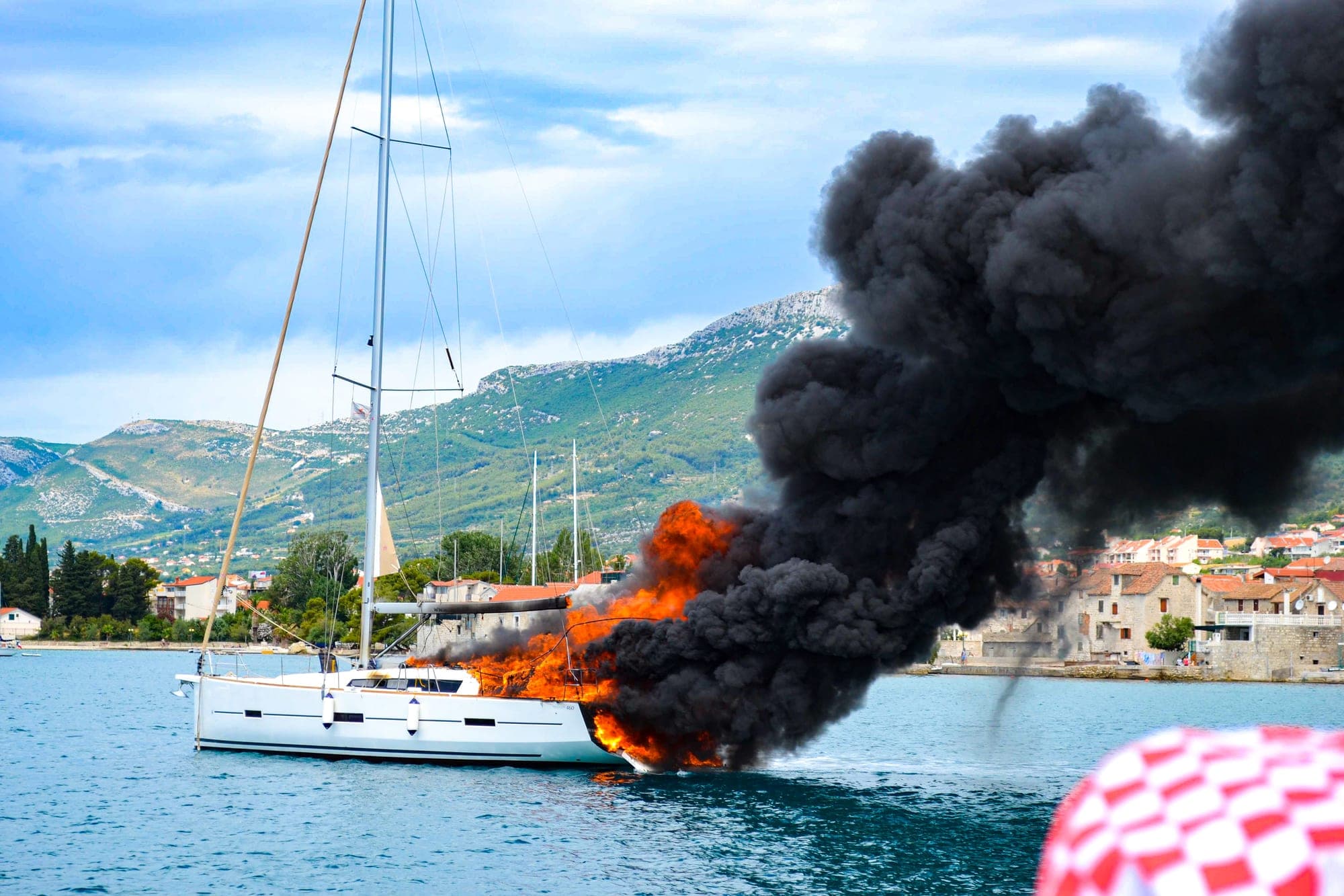 Sailing yacht burning with thick black smoke near shore