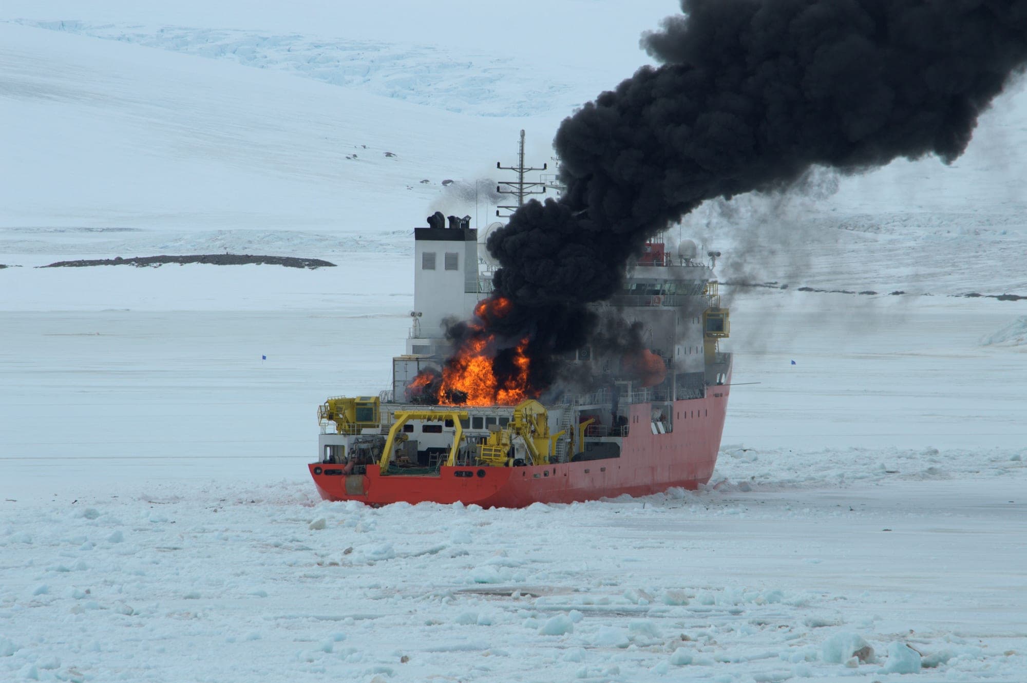 Cargo ship burning amid pack ice with heavy black smoke