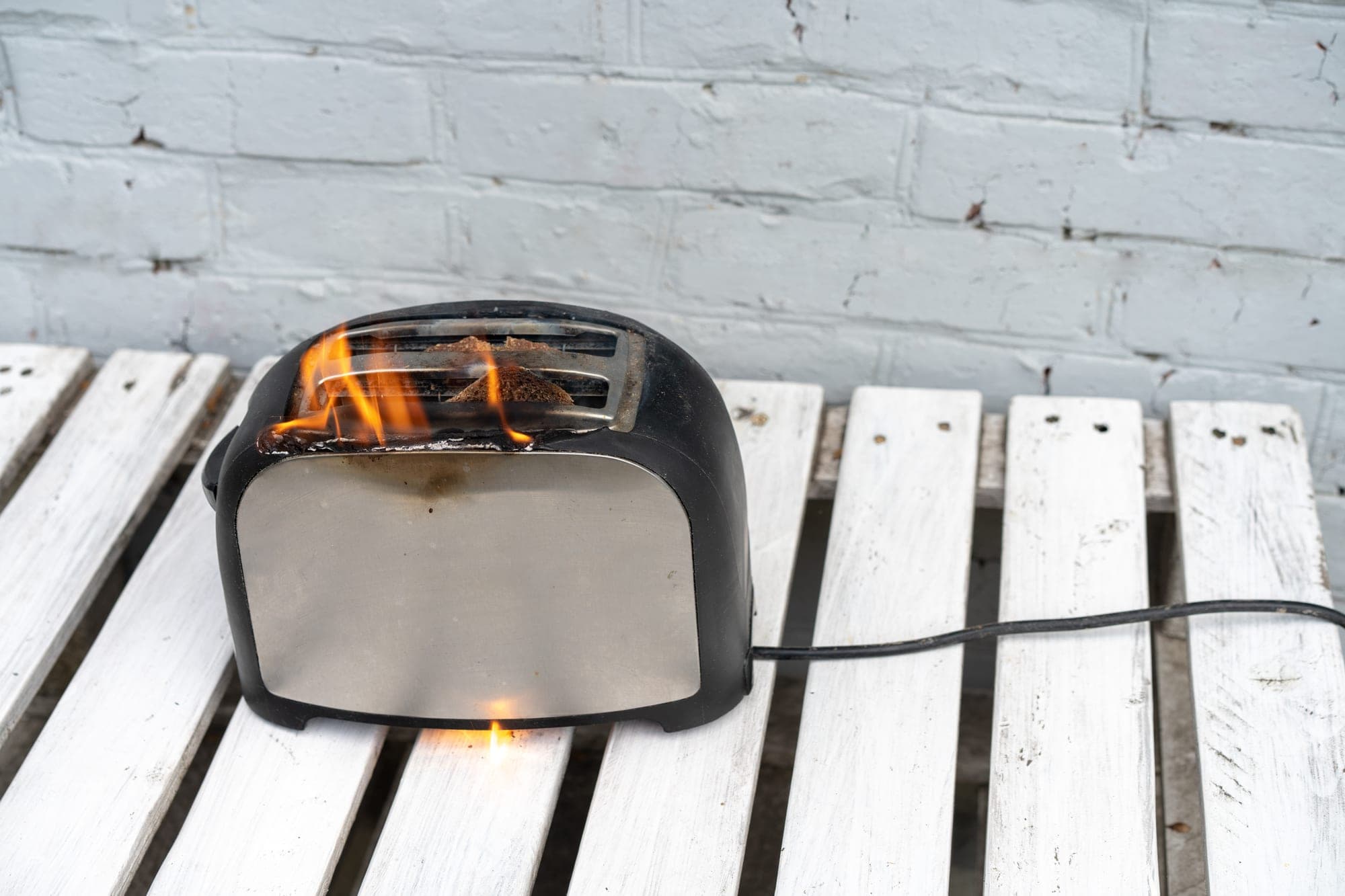 Toaster on fire on an outdoor wooden bench