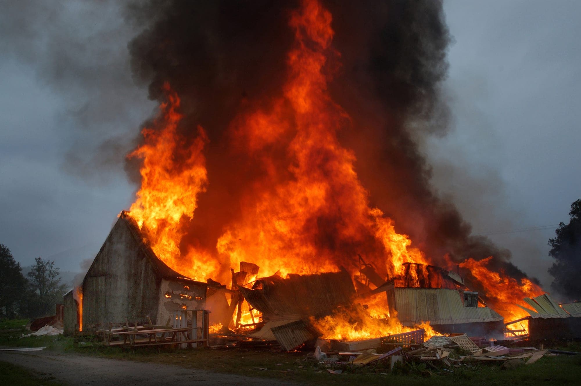 Farm outbuildings fully engulfed in towering flames