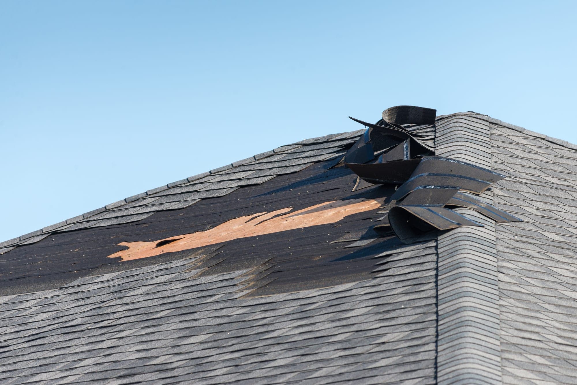 Wind-torn shingles peeled back at a roof ridge