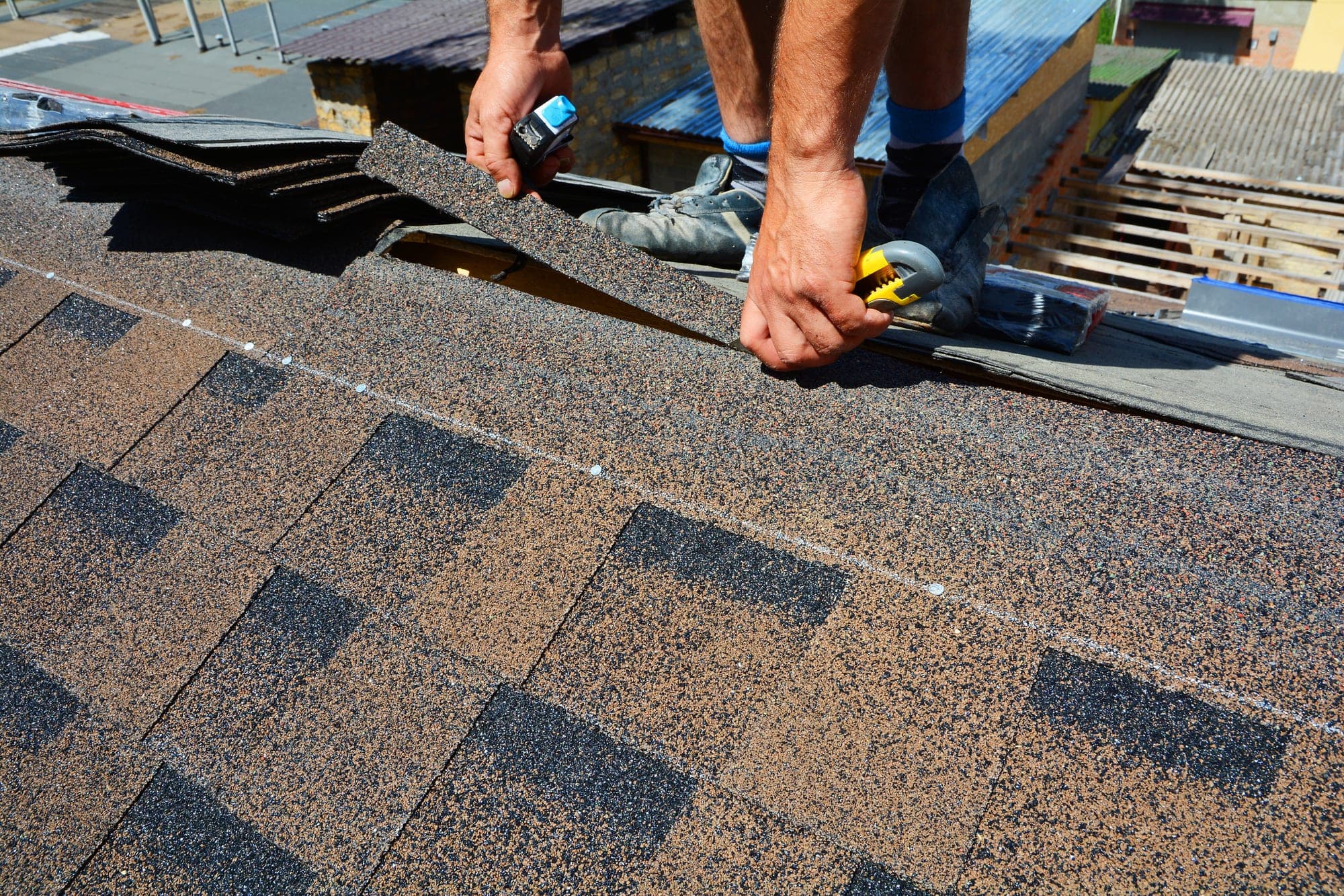 Roofer's hands working shingles at a roof ridge