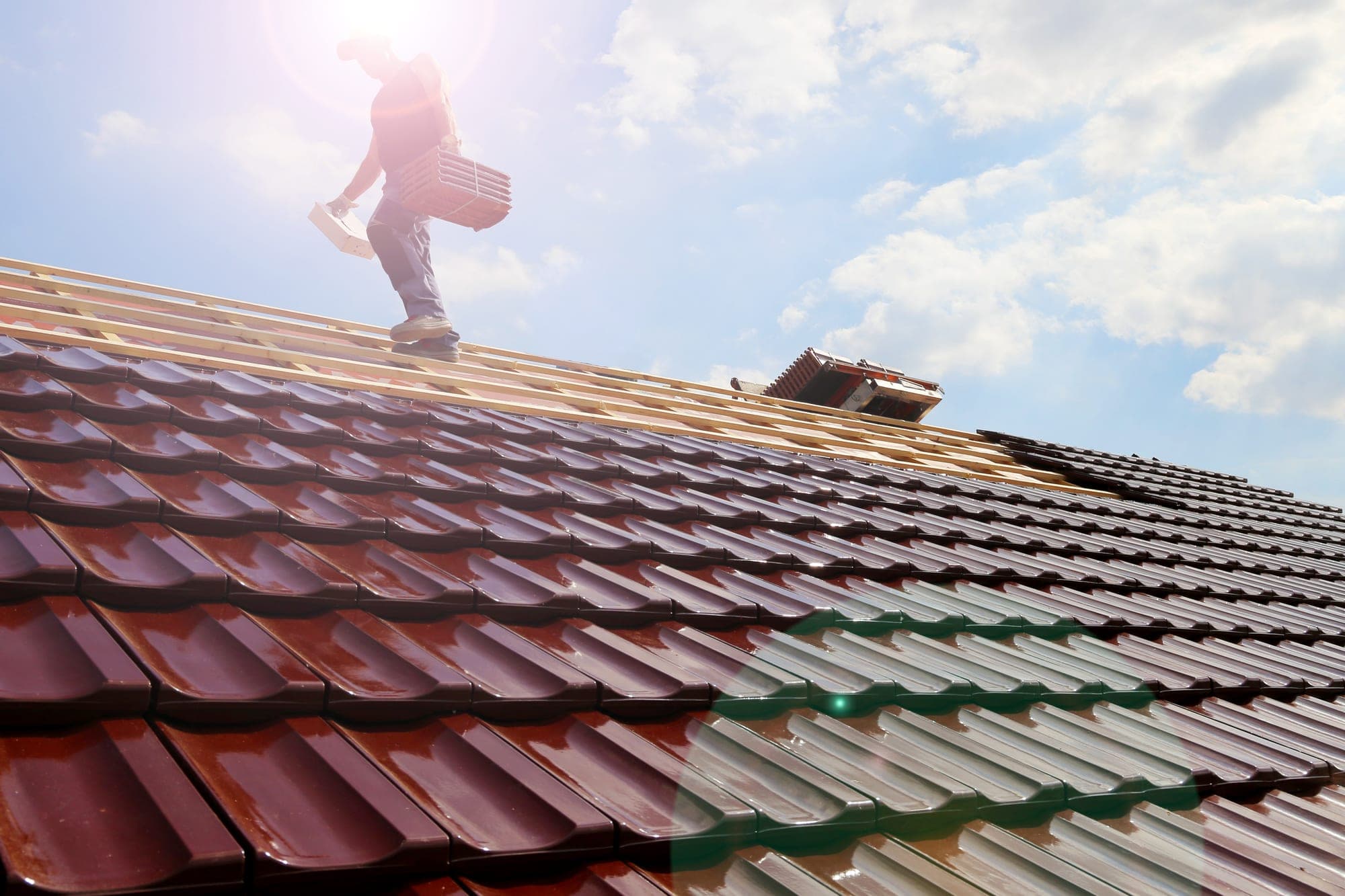 Roofer carrying tiles across a roof under construction
