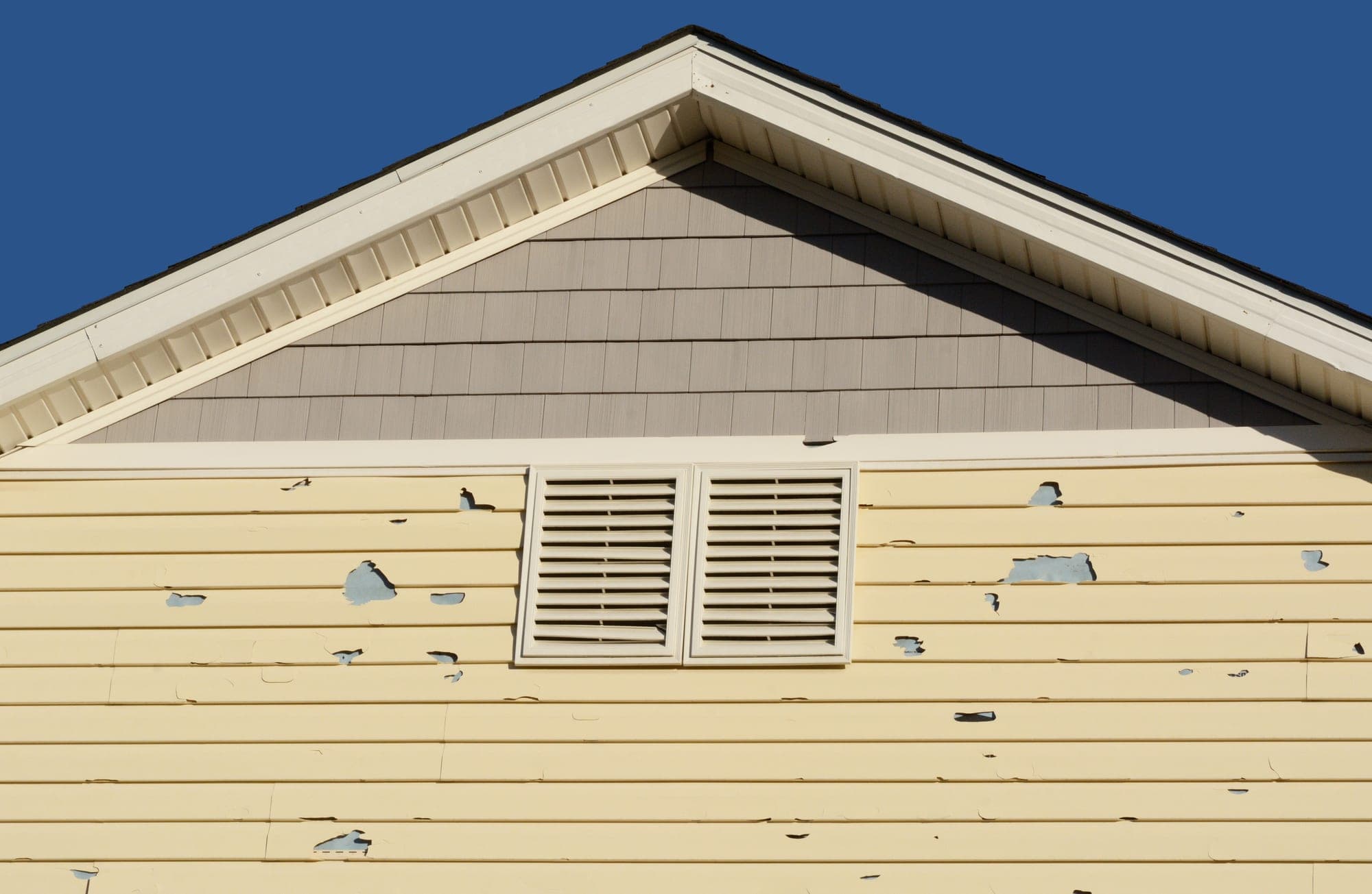Hail impact marks pocking the vinyl siding of a home