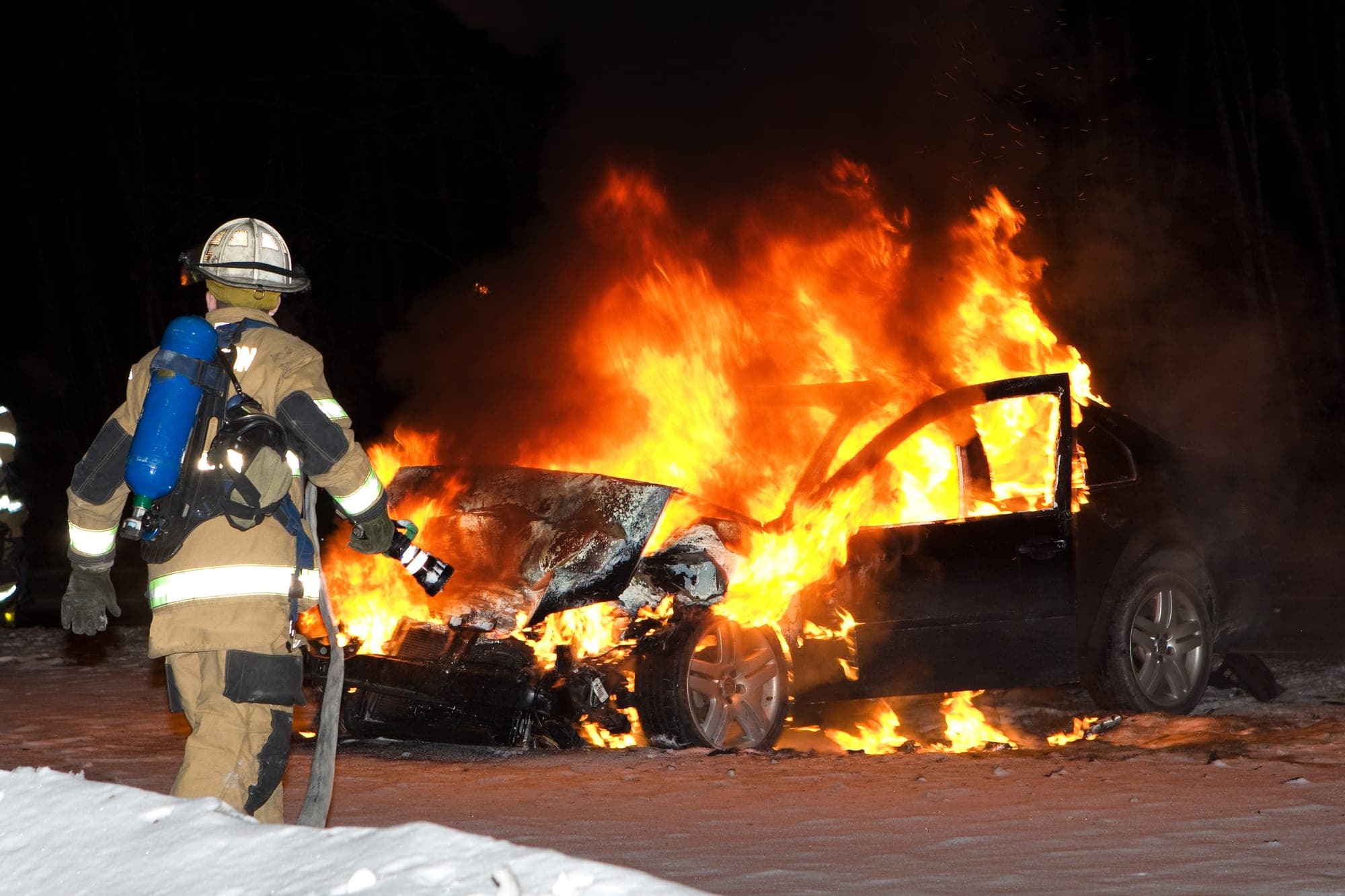 Firefighter approaching a burning sedan on a snowy night
