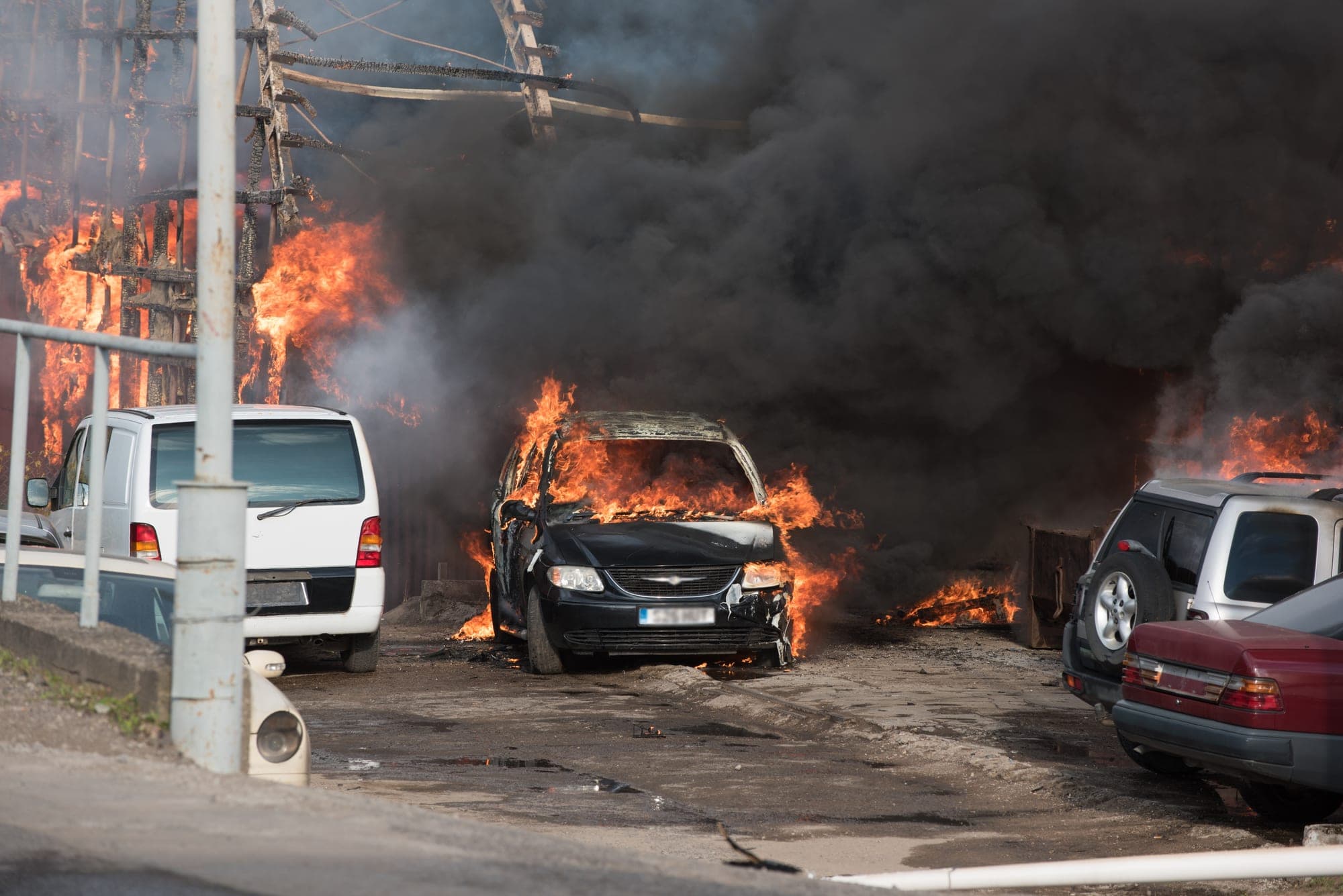 Minivan burning in a lot near a fire-damaged structure