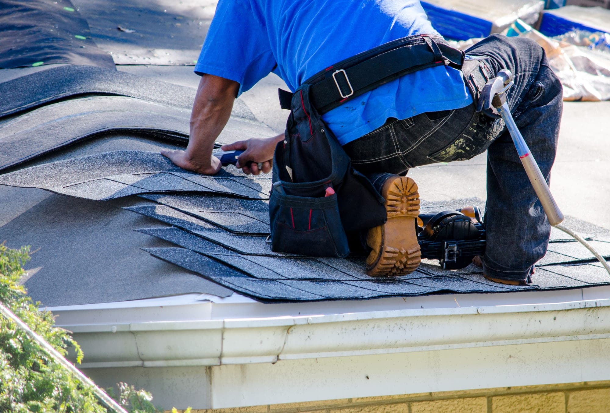 Roofer kneeling at a roof edge repairing asphalt shingles